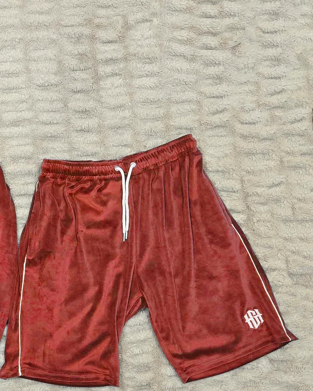 Red velour shorts laid flat, with white piping, a white drawcord and an HGH monogram on the leg